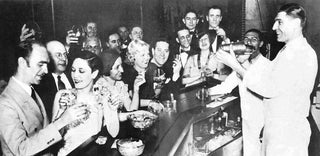 Black and white photo of a group of smiling people toasting drinks at a crowded bar, with a bartender serving them.