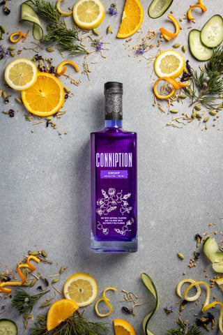 Conniption Kinship gin surrounded by botanicals and sliced oranges and cucumber